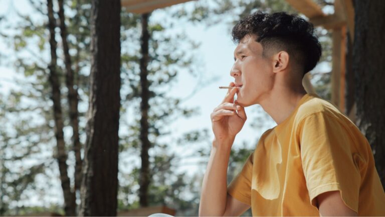 Man leaning against a tree smoking a cannabis pre-roll