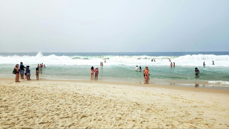 Beachgoers in the sand and ocean as waves crash in the distance.