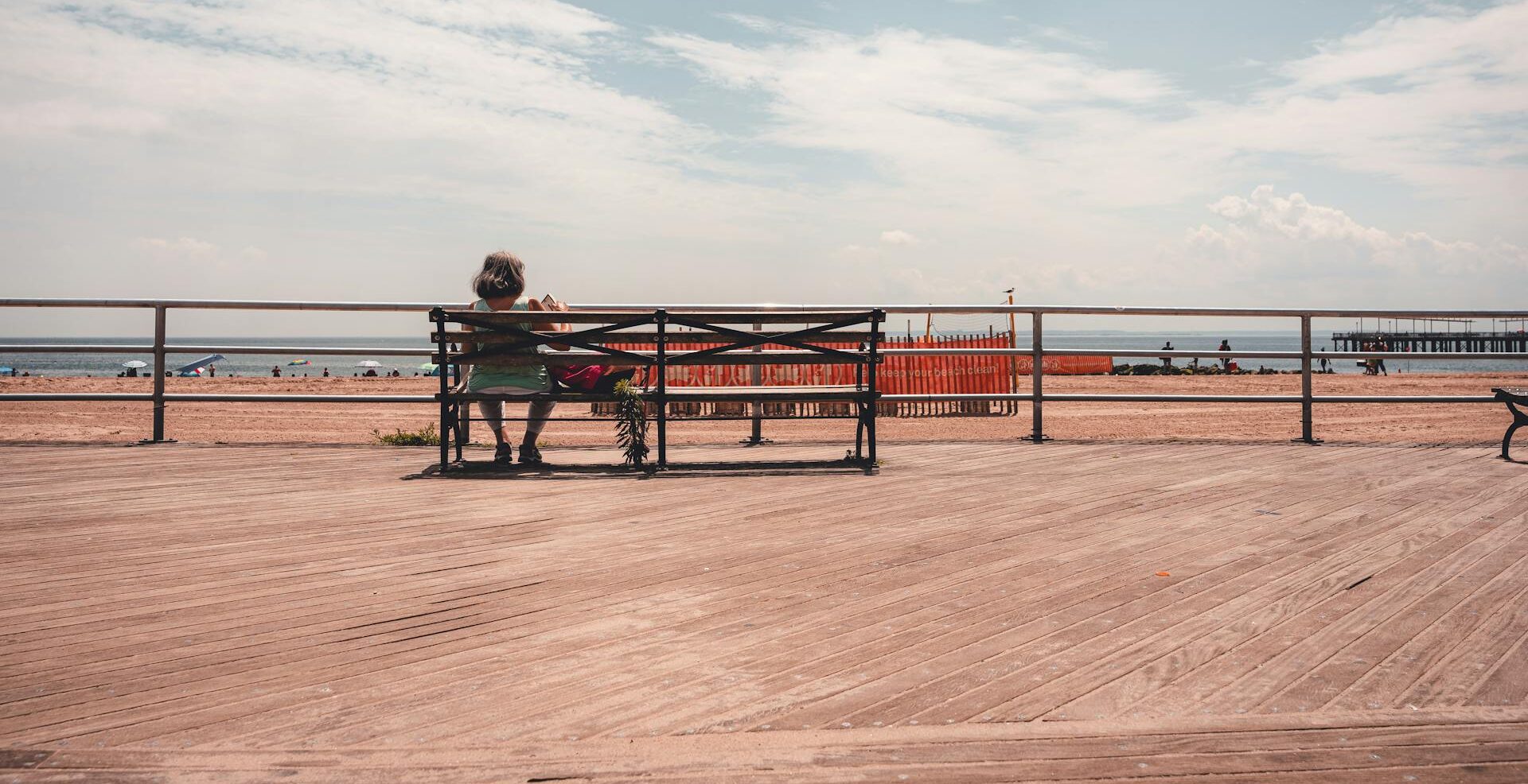 woman sitting on a bench on a boardwalk facing the sea. Source - Pexels