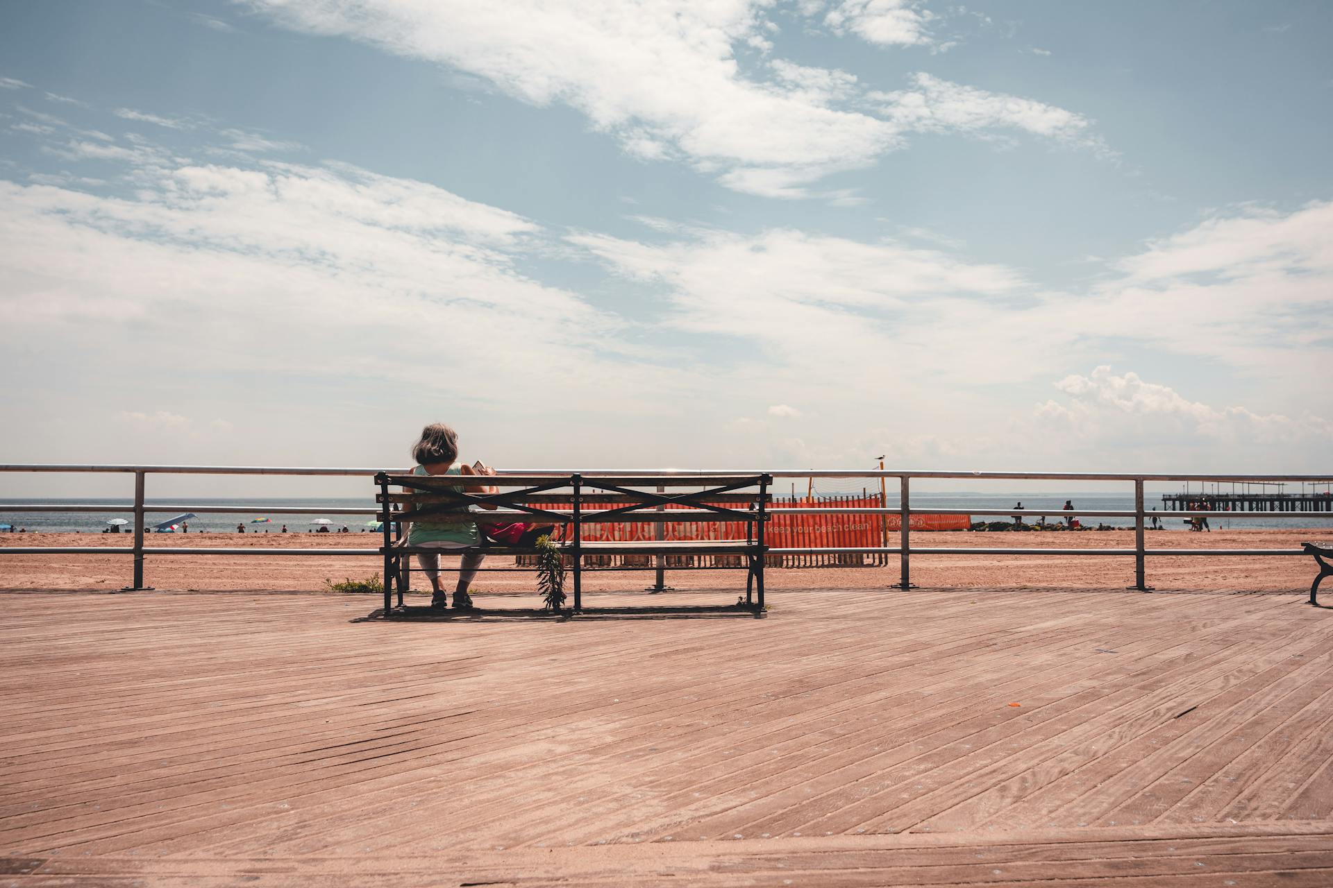 woman sitting on a bench on a boardwalk facing the sea. Source - Pexels